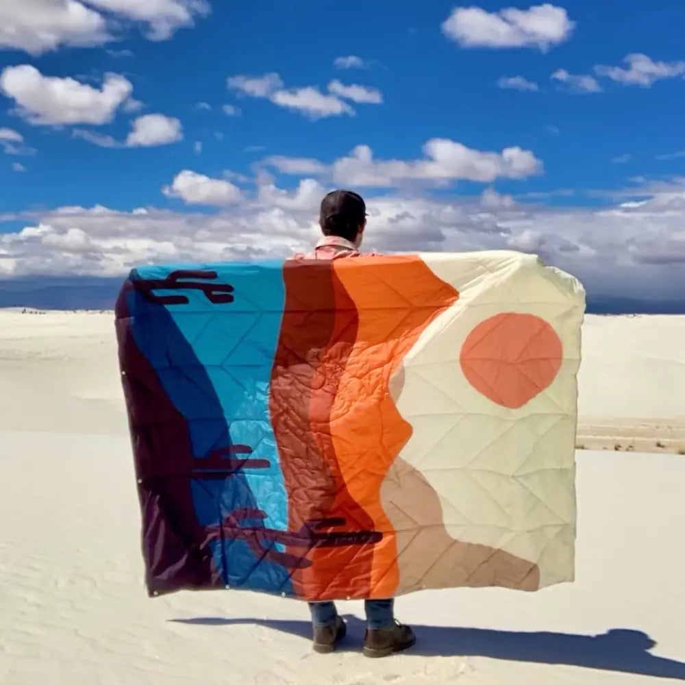 Man holding a colorful DryFox blanket in Nature print against a blue sky with clouds