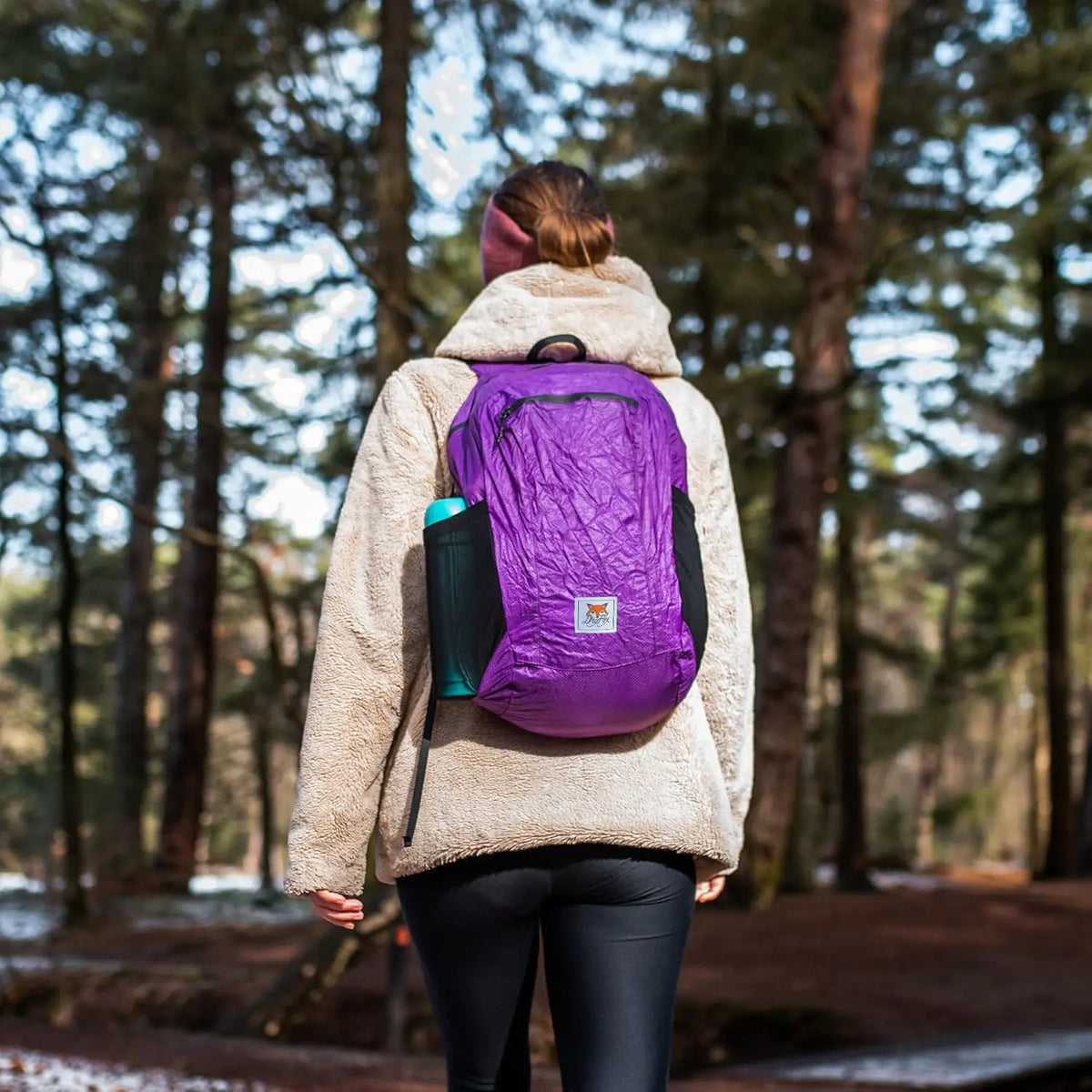 Person wearing a purple backpack in a forest