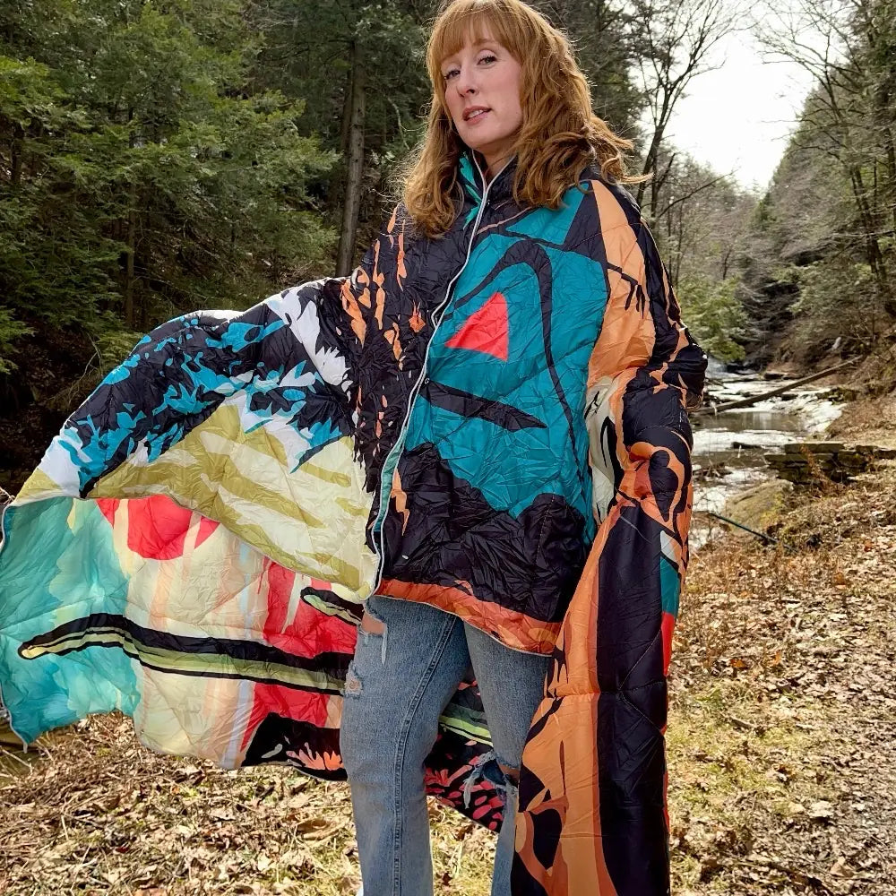 Woman wearing a colorful DryFox blanket in Campout print in a forest setting